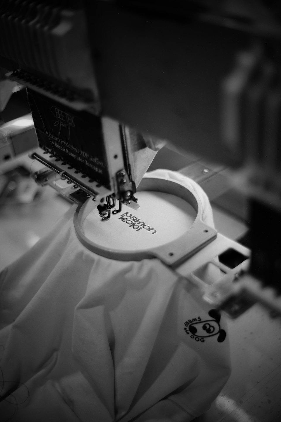An industrial embroidery machine stitches text onto stretched fabric.