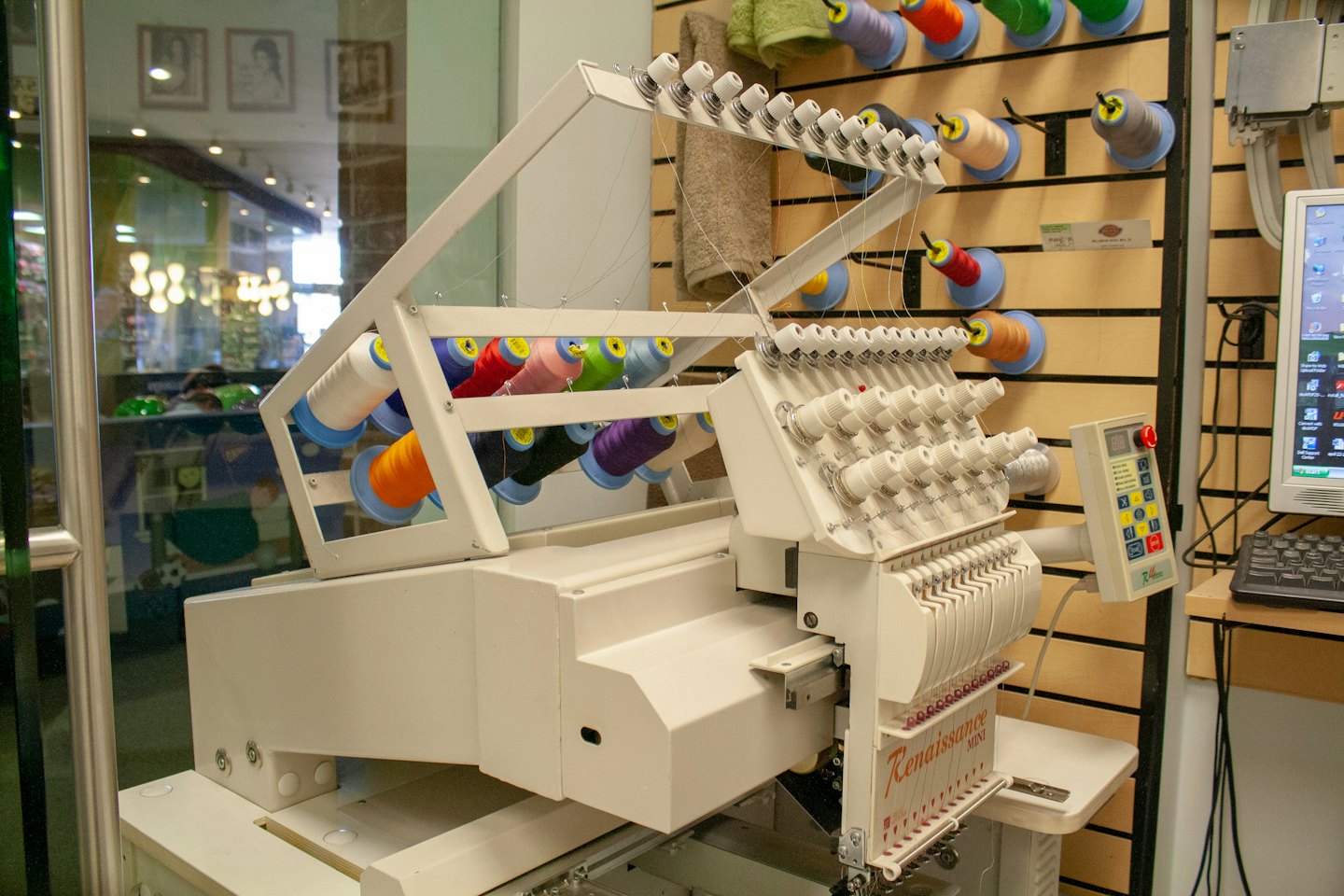 Multi-needle embroidery machine with colorful thread spools in a workshop.