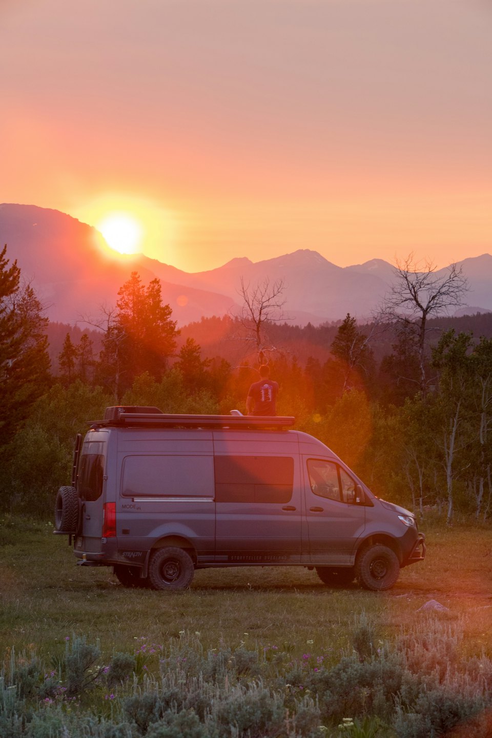 Person sits on top of a camper van watching the sunset.